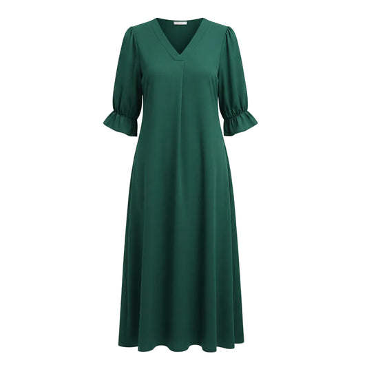 Woman wearing a green dress with puff sleeves against a white wall.