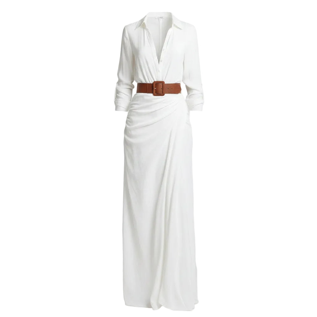 Woman wearing a white dress with a brown belt and holding a woven bag against a plain background