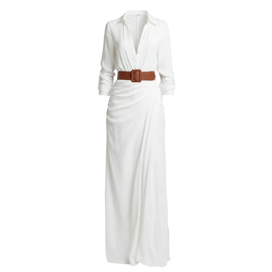 Woman wearing a white dress with a brown belt and holding a woven bag against a plain background