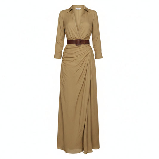 A woman models a flowing tan maxi shirt dress with a deep V-neck, long sleeves rolled to the forearm, and a brown leather belt. She is carrying a woven straw tote bag and wearing flat brown sandals, set against a textured light gray concrete wall.