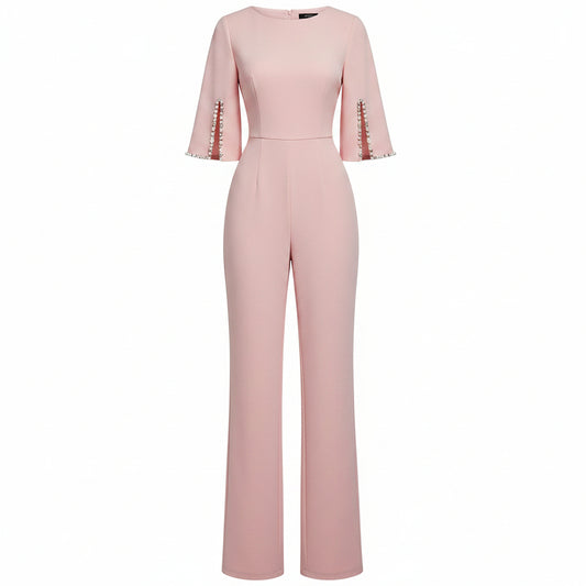 Woman wearing a pink jumpsuit with pearl embellishments against a plain background