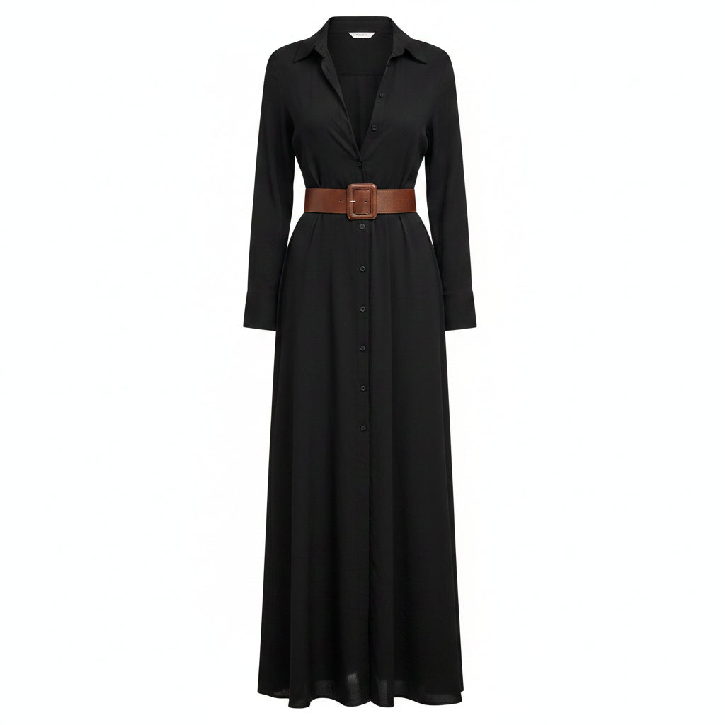 A woman models a long black button-front shirt dress with a deep V-neck, long sleeves, and a matching long skirt. She wears a brown belt with a large square buckle at the waist and carries a woven straw tote bag against a textured light gray wall.
