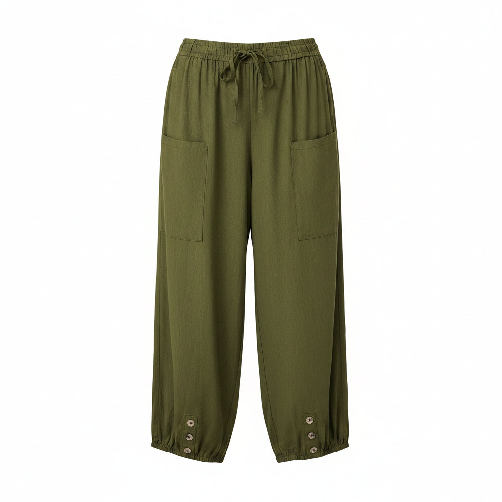 A person wearing olive green drawstring cropped pants with side pockets and button details at the cuffs, paired with a light blue top and beige slide sandals in a bright indoor setting.
